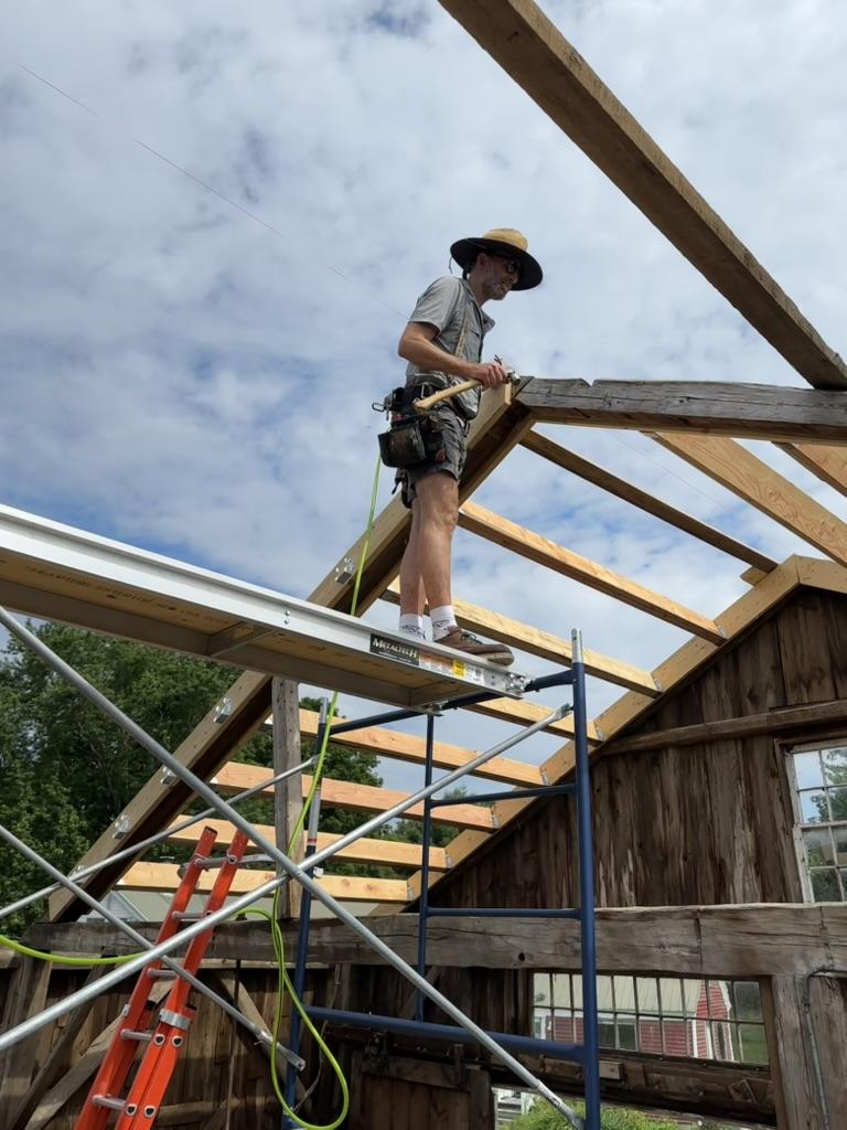 Dave on scaffolding framing the barn roof against an open summer sky